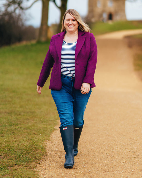 Woman in a purple coat, striped shirt, and blue jeans walking on a path outdoors.. This blazer is the Auburn Blazer sewing pattern from Cashmerette.