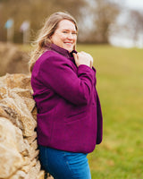 Woman in a purple coat standing next to a stone wall with a blurred natural background. This blazer is the Auburn Blazer sewing pattern from Cashmerette.