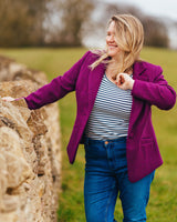 Woman in a purple coat standing next to a stone wall in a field. This blazer is the Auburn Blazer sewing pattern from Cashmerette.