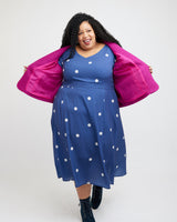 Woman wearing a blue dress with white polka dots and a pink jacket on a white background. This blazer is the Auburn Blazer sewing pattern from Cashmerette.