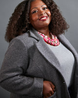 Woman wearing a gray coat and pink necklace against a gray background. This blazer is the Auburn Blazer sewing pattern from Cashmerette.