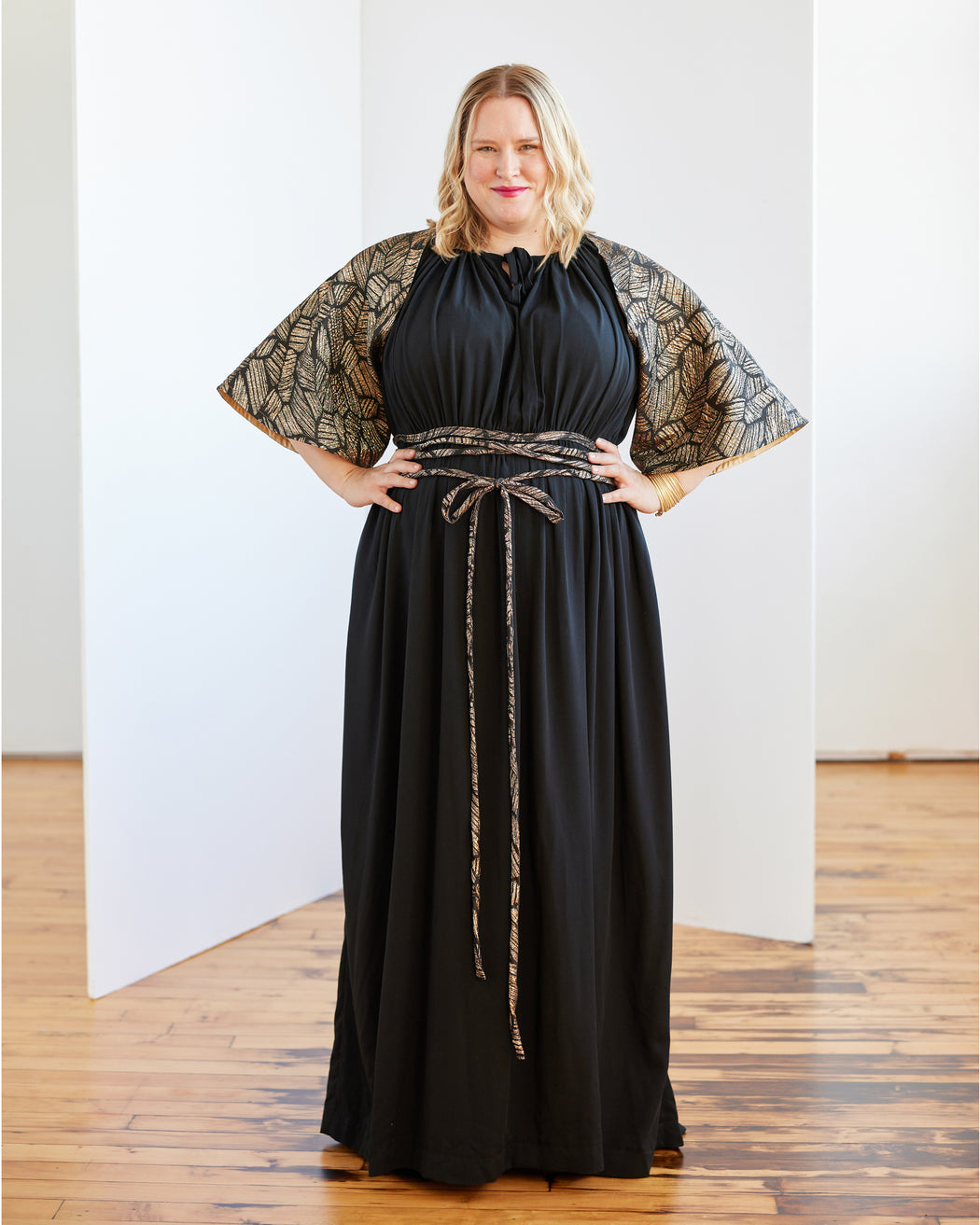 Woman wearing a black dress with lace sleeves against a white background. The topper is the Caroll Shrug sewing pattern from Cashmerette.