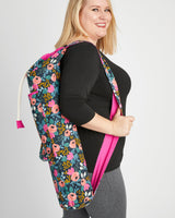 Woman holding a floral-patterned bag against a plain background. This yoga bag is the Shawmut Yoga Bag sewing pattern from Cashmerette.