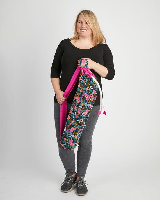 Woman holding a floral yoga bag with pink strap on a white background. This yoga bag is the Shawmut Yoga Bag sewing pattern from Cashmerette.