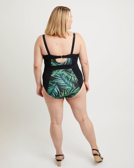 Woman wearing a black swimsuit with green leaf pattern on a white background. This swimsuit is the Ipswich Swimsuit sewing pattern from Cashmerette.