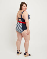 Woman wearing a navy and white striped swimsuit with a red belt on a white background. This swimsuit is the Ipswich Swimsuit sewing pattern from Cashmerette.