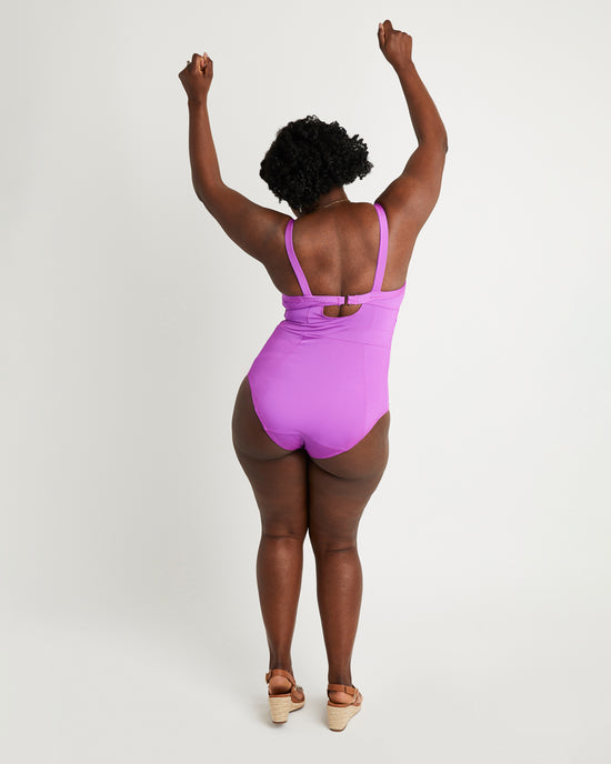Person wearing a purple swimsuit with arms raised on a white background. This swimsuit is the Ipswich Swimsuit sewing pattern from Cashmerette.