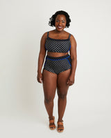 Woman wearing a black and white polka dot bikini with blue accents on a white background. This swimsuit is the Ipswich Swimsuit sewing pattern from Cashmerette.