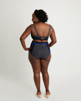 Woman wearing a black and white polka dot swimsuit with blue trim on a white background. This swimsuit is the Ipswich Swimsuit sewing pattern from Cashmerette.