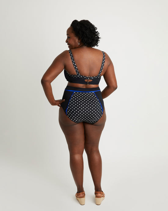 Woman wearing a black and white polka dot swimsuit with blue trim on a white background. This swimsuit is the Ipswich Swimsuit sewing pattern from Cashmerette.