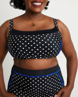 Woman wearing a black and white polka dot top with blue accents on a plain background. This swimsuit is the Ipswich Swimsuit sewing pattern from Cashmerette.