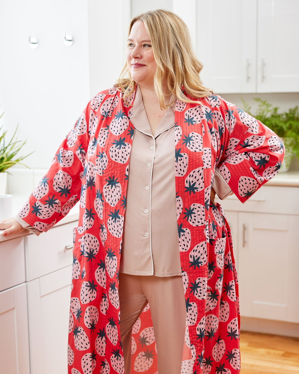 Woman wearing a red strawberry patterned robe in a kitchen. This robe is the Lygon Robe sewing pattern from Cashmerette.