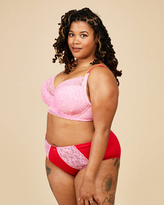 Woman wearing a pink lace bra and red underwear against a beige background. These undies are the Radcliffe Undies sewing pattern from Cashmerette.