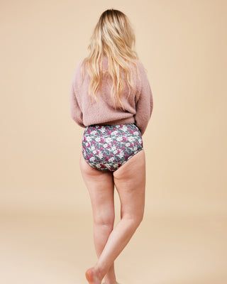 Person wearing floral underwear and a pink sweater on a beige background. These undies are the Radcliffe Undies sewing pattern from Cashmerette.