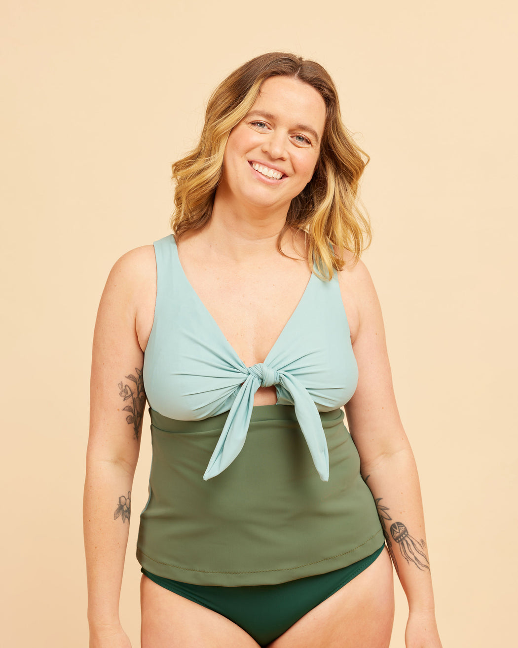 Woman wearing a green and light blue tankini set on a beige background. This swimsuit is the Marblehead Swimsuit sewing pattern from Cashmerette.