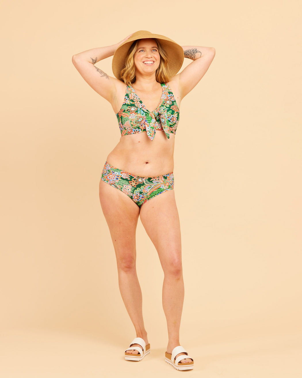 Woman wearing a floral bikini and wide-brimmed hat on a beige background. This swimsuit is the Marblehead Swimsuit sewing pattern from Cashmerette.