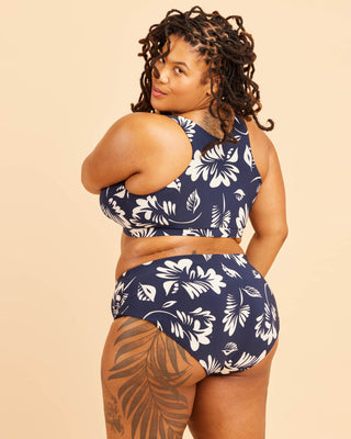 Woman wearing a navy blue bikini with white floral patterns on a beige background. This swimsuit is the Marblehead Swimsuit sewing pattern from Cashmerette.