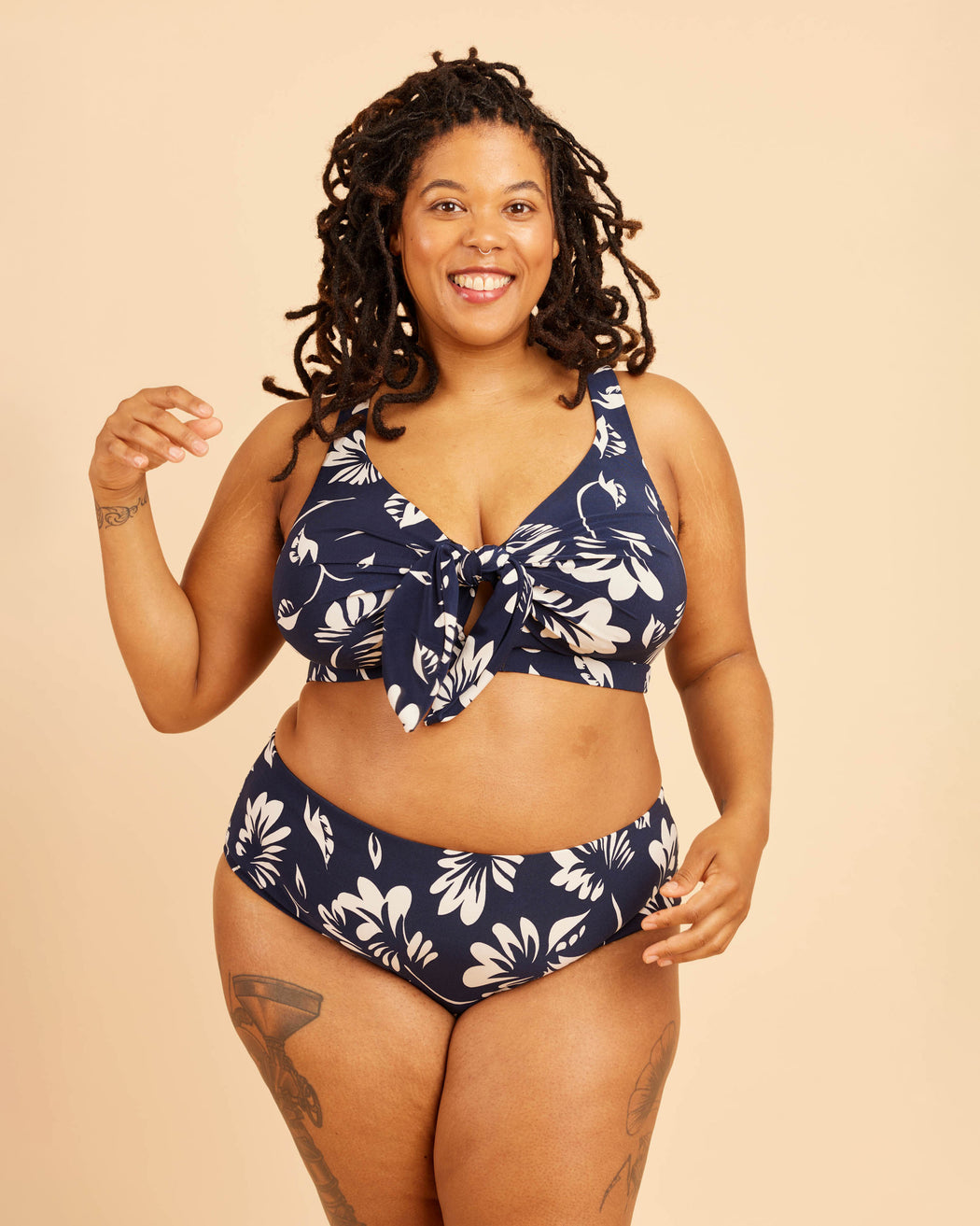 Woman wearing a navy blue bikini with white floral patterns on a beige background. This swimsuit is the Marblehead Swimsuit sewing pattern from Cashmerette.