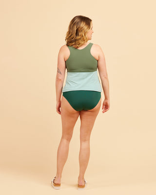 Woman wearing a green and light blue swimsuit on a beige background. This swimsuit is the Marblehead Swimsuit sewing pattern from Cashmerette.