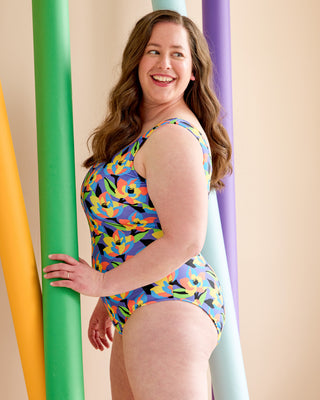Woman wearing a colorful swimsuit standing against a pastel-colored curtain. This is the Truro Swimsuit sewing pattern from Cashmerette.
