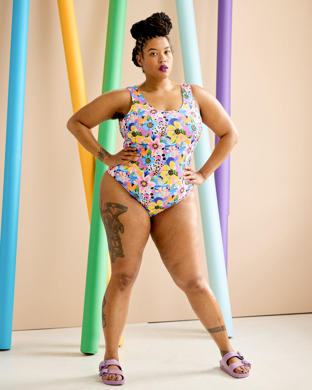 Woman wearing a colorful floral swimsuit standing in front of colorful cylindrical objects. This is the Truro Swimsuit sewing pattern from Cashmerette.