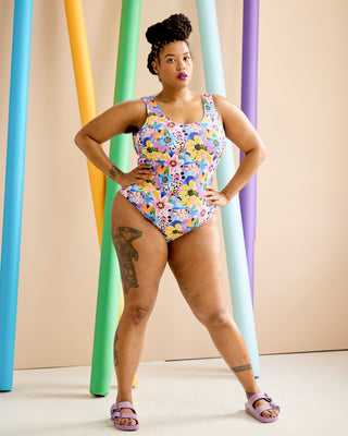Woman wearing a colorful floral swimsuit standing in front of colorful cylindrical objects. This is the Truro Swimsuit sewing pattern from Cashmerette.