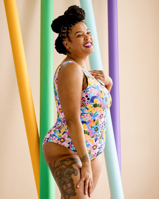 Woman wearing a colorful floral swimsuit against a pastel background. This is the Truro Swimsuit sewing pattern from Cashmerette.