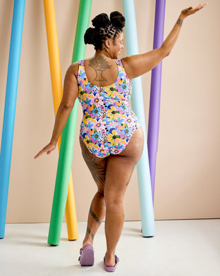 Woman wearing a colorful floral swimsuit standing in front of vertically arranged colorful tubes. This is the Truro Swimsuit sewing pattern from Cashmerette.