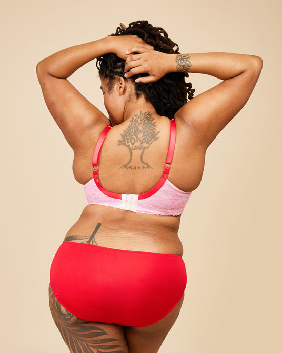 Person wearing a pink bikini top and red bottoms against a beige background. This bra is the Willowdale Bra sewing pattern from Cashmerette.