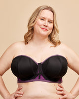 Woman wearing a black and purple strapless bra against a beige background. This bra is the Symmes Strapless Bra sewing pattern from Cashmerette.