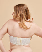 Woman wearing a white strapless top against a beige background. This bra is the Symmes Strapless Bra sewing pattern from Cashmerette.