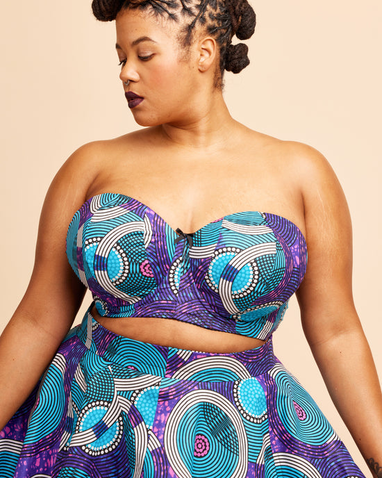Woman wearing a strapless top and skirt with a purple and blue pattern on a beige background. This bra is the Symmes Strapless Bra sewing pattern from Cashmerette.