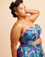 Woman wearing a colorful strapless top and skirt set against a beige background. This bra is the Symmes Strapless Bra sewing pattern from Cashmerette.