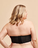 Woman wearing a black strapless top against a beige background. This bra is the Symmes Strapless Bra sewing pattern from Cashmerette.