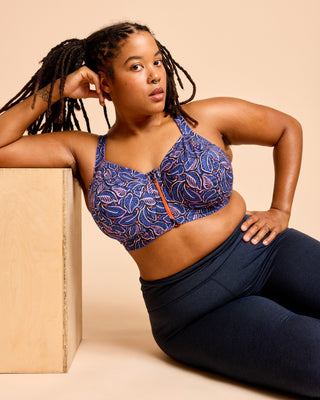 Woman wearing a blue patterned sports bra and navy leggings against a beige background. This is the Cashmerette Somerville Sports Bra sewing pattern for big boobs.