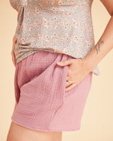 Person wearing a floral top and pink shorts on a beige background. This is the Fiske Sleepwear Set sewing pattern from Cashmerette.