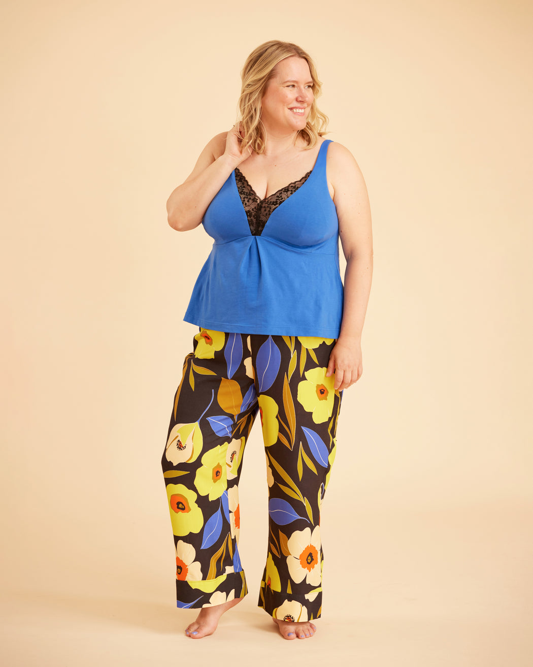 Woman wearing a blue top and floral pants on a beige background. This is the Fiske Sleepwear Set sewing pattern from Cashmerette.