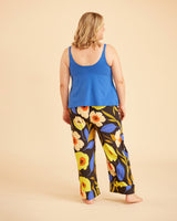 Woman wearing a blue tank top and colorful floral pants on a beige background. This is the Fiske Sleepwear Set sewing pattern from Cashmerette.
