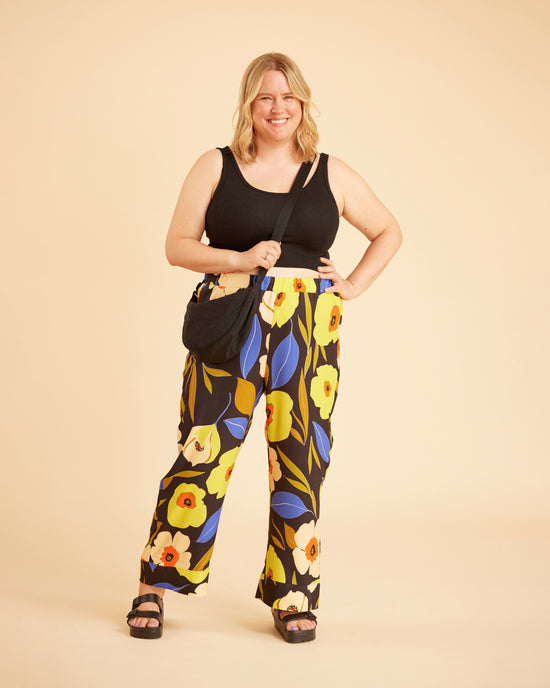 Woman wearing a black tank top and floral pants against a beige background. This is the Fiske Sleepwear Set sewing pattern from Cashmerette.