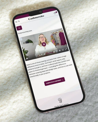 Phone laying on a textured white background, showing a screenshot of a lesson from Cashmerette Fitting University.