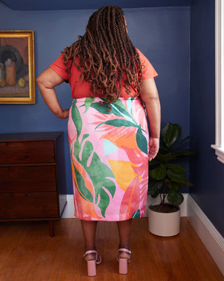 Person wearing a red top and pink skirt with leaf pattern in a room with blue walls and wooden floor. This skirt is the Randolph Wrap Skirt sewing pattern from "Sewing the Curve" by Jenny Rushmore.