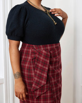 Person wearing a black top and red plaid skirt against a white background. This skirt is the Randolph Wrap Skirt sewing pattern from "Sewing the Curve" by Jenny Rushmore.