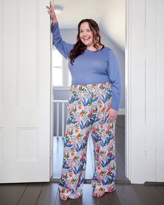 Woman wearing a blue top and colorful floral pants standing in a doorway. These pants are the Ardley Elastic Waist Pants sewing pattern from "Sewing the Curve" by Jenny Rushmore.