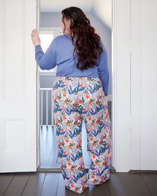 Woman wearing a blue top and colorful floral pants standing in a doorway. These pants are the Ardley Elastic Waist Pants sewing pattern from "Sewing the Curve" by Jenny Rushmore.