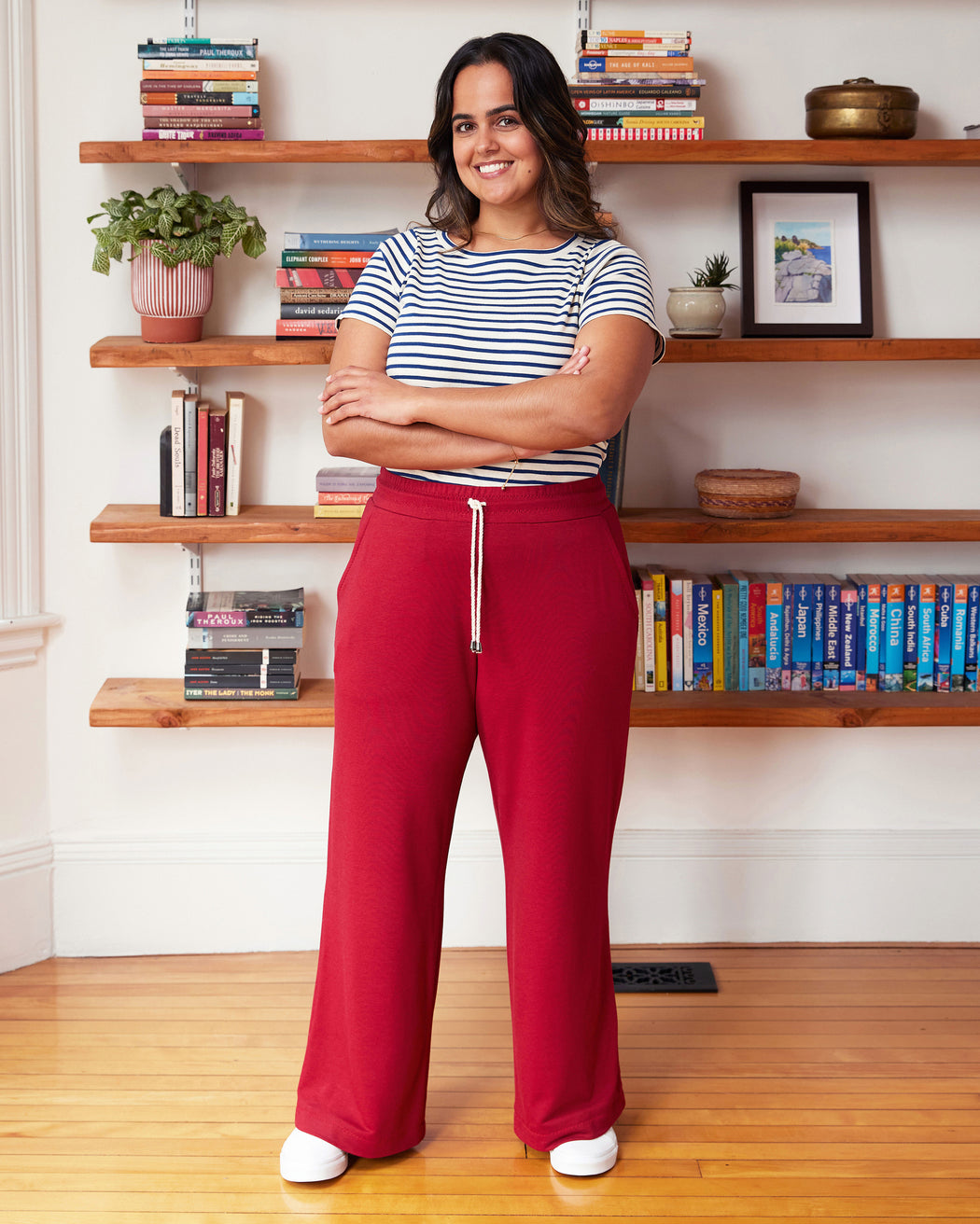 Woman in striped shirt and red pants standing in a room with wooden shelves and books. These pants are the Ardley Elastic Waist Pants sewing pattern from "Sewing the Curve" by Jenny Rushmore.