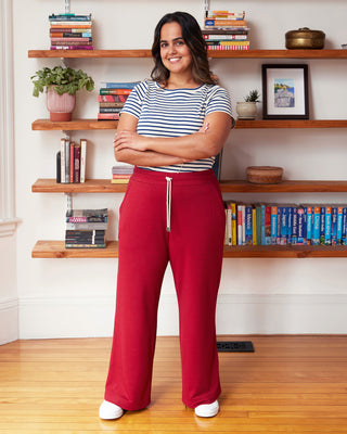 Woman in striped shirt and red pants standing in a room with wooden shelves and books. These pants are the Ardley Elastic Waist Pants sewing pattern from "Sewing the Curve" by Jenny Rushmore.