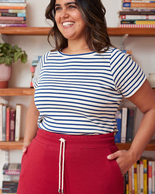 Woman wearing a striped shirt and red pants standing in front of a bookshelf. This top is the Eustis T-Shirt sewing pattern from "Sewing the Curve" by Jenny Rushmore.