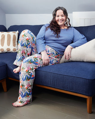 Woman sitting on a blue sofa wearing colorful pants and a blue top. These pants are the Ardley Elastic Waist Pants sewing pattern from "Sewing the Curve" by Jenny Rushmore.
