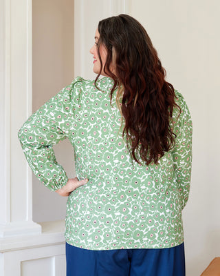 Woman wearing a green floral blouse with blue pants indoors. This top is the Eustis T-Shirt sewing pattern from "Sewing the Curve" by Jenny Rushmore.