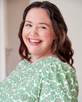 Woman wearing a green floral patterned shirt with a blurred background. This top is the Eustis T-Shirt sewing pattern from "Sewing the Curve" by Jenny Rushmore.